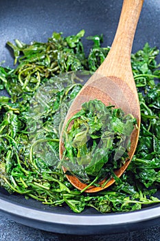 Wilted arugula or rocket salad, preparing a side dish in frying pan, vertical