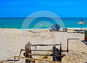 A winch pulling two old wooden row-boats of different sizes on the sandy beach of the Black Sea on a clear, blue sky, sunny summer