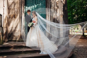 Wind blows bride& x27;s veil while she stands with groom