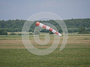 Wind direction and strength indicator on the airfield on a sunny summer day. Synthetic product made of red and white