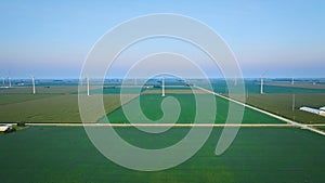 Wind farm in early morning with green fields and crops in farmland aerial