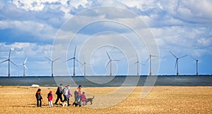 Wind farm off the coast of Yarmouth with family walking dogs on beach in Great Yarmouth, Norfolk, UK