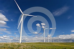 Wind farm turbines white on hill contrast green grass and blue sky, wa