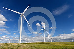 Wind farm turbines white on hill contrast green grass and blue sky, wa