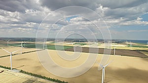 Wind farms in rural areas against the background of agricultural fields under a blue sky. Aerial survey
