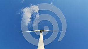 Wind generator against a blue sky with clouds. Rotation of white wind turbine blades