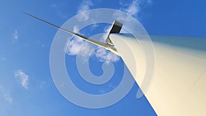 Wind generator against a blue sky with clouds. Rotation of white wind turbine blades