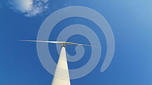 Wind generator against a blue sky with clouds. Rotation of white wind turbine blades