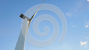 Wind generator against a blue sky with clouds. Rotation of white wind turbine blades