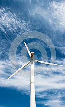 Wind generator of electricity from three blades against the background of clouds and blue sky