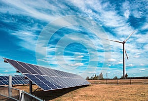 Wind generator of electricity from three blades and solar panel batteries of photocells against a background of clouds and sky