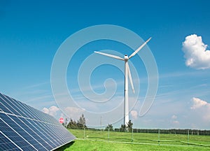 Wind generator of electricity from three blades and solar panels background of clouds and a blue sky green grass