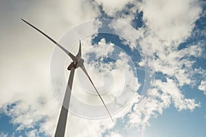 Wind generator propeller against blue cloudy sky. Shot from the ground to the sky. Renewable energy concept. Blue and white color