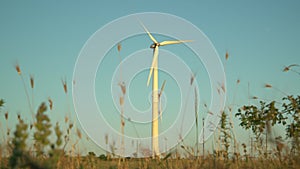 A wind generator slowly spins its blades in a field at sunset