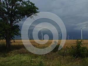 Wind generators are built on a wheat field against the background of a stormy sky