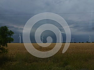 Wind generators are built on a wheat field against the background of a stormy sky