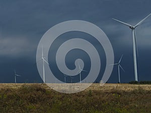 Wind generators are built on a wheat field against the background of a stormy sky