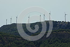 Wind generators stand in a row on a wooded mountaintop