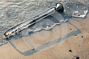 Wind instrument lies in the water on a sandy beach, summer lyric concept, closeup