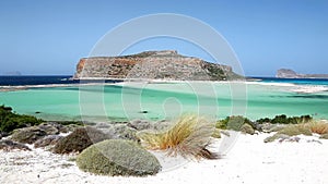Wind moving the grassland on white sands of Balos beach lagoon on Crete, Greece. Gramvousa island can be seen in the
