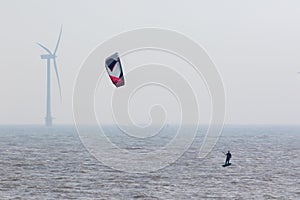 Wind power. Kitesurfer surfing by offshore windfarm turbine. Green energy