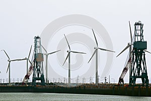 Wind power station on the pier with the port cranes