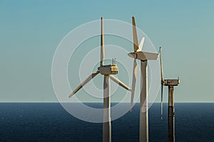 Wind power stations. A row of turbines near the seashore. Wind farm eco field. Eolic park with blue sky in background. Green,