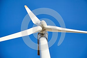 Wind power turbine against a blue sky background. White blades of a wind generator closeup. Renewable energy source.