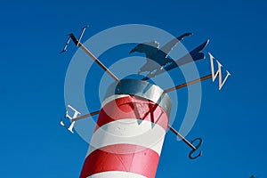 A wind rose with a tin eagle on a tall red and white pole with a beautiful clear blue summer sky in the background