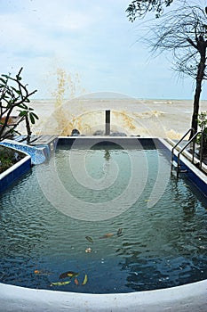 Wind and sea waves crash against the swimming pool line in the seaside resort