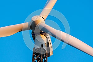 Wind turbine against a clear blue sky at a wind turbine farm at sunset. Low angle view, close-up on propeller. Sustainable energy.
