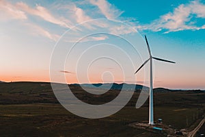 Wind turbine, alternative energy, wind energy, one windmill in a field in the mountains, top view of a wind turbine at sunset