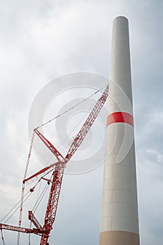 Wind turbine construction site, turbine tower with crane next to it, view from low angle during cloudy day