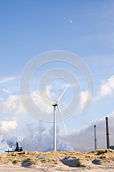 Wind turbine with factory smoke against cloudy pastel coloured sky at the sand dunes