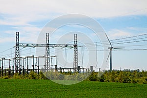 Wind turbine farm and substation electricity power transmission lines in landscape with green grass and blue sky