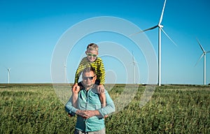 Wind turbine field. Father carrying son on shoulders and waving their arms like a windmill.