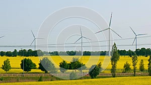 Wind turbine on grassy yellow farm canola field against cloudy blue sky in rural area. Concept of climate friendly