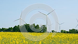Wind turbine on grassy yellow farm canola field against cloudy blue sky in rural area. Concept of climate friendly