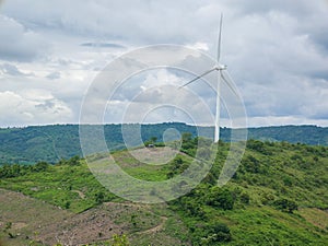 A wind turbine on the green hilly terrain with the bright blue sky