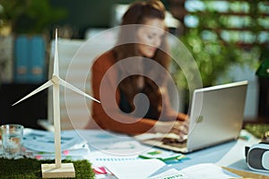 Wind turbine in green office and woman with laptop working