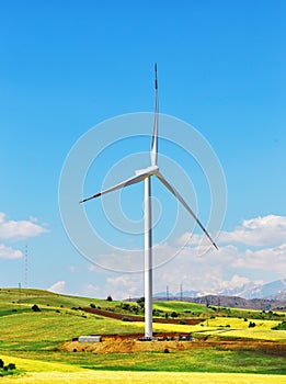 Wind turbine on hill against blue sky