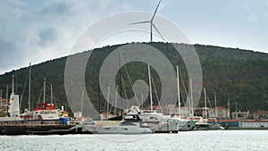Wind turbine located on the hill top next to the sea port with moored yachts, ships and boats. Concept of green electricity.