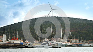 Wind turbine located on the hill top next to the sea port with moored yachts, ships and boats. Concept of green electricity,