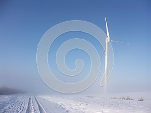 Wind turbine in misty snowy landscape against blue sky