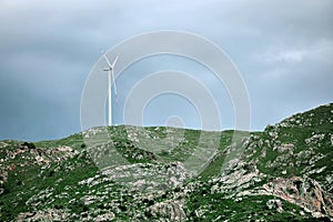 Wind turbine over a rocky mountaintop covered with green plants