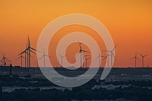 Wind turbine power generators silhouettes at ocean coastline at sunset. Alternative renewable energy production