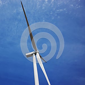 Wind turbine producing alternative energy on the background of blue sky.