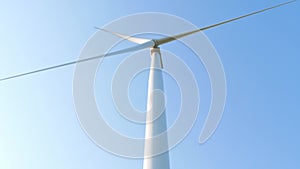 Wind turbine rotating on clear blue sky background. Local eco friendly energy wind converter farm. Green electricity