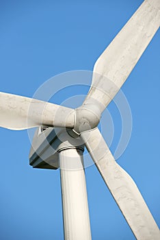 A wind turbine and rotor blades isolated against a blue sky on a sustainable, eco friendly farm. Low angle view of