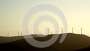 Wind turbine silhouettes on top of a hill at golden hour